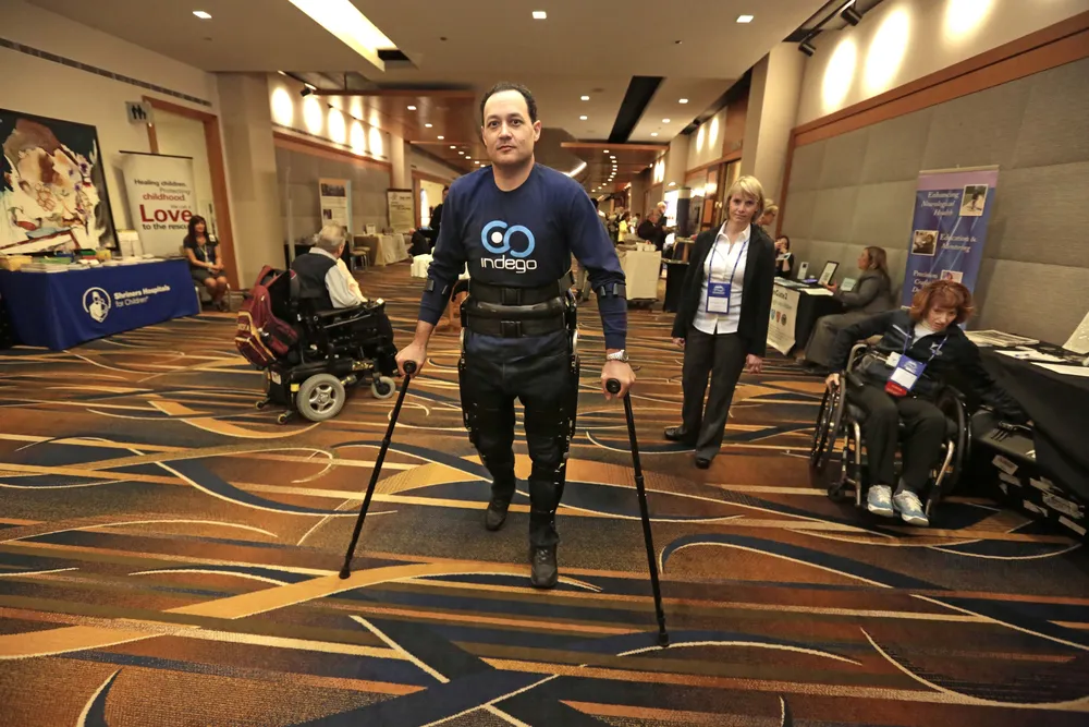 Michael Gore, quien sufre de una parálisis debido a una lesión en la espina dorsal, camina utilizando las piernas electrónicas de Indego bajo la supervisión de la terapeuta Clare Hartigan