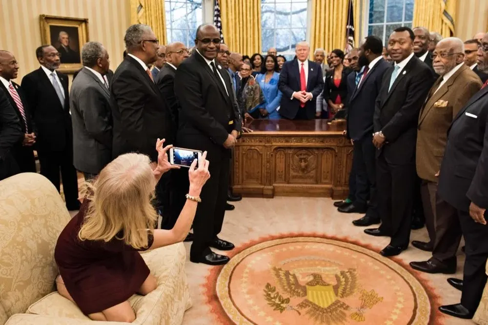 Conway, arrodillada, toma la foto de Trump con líderes de universidades y colegios negros históricos en la oficina oval.