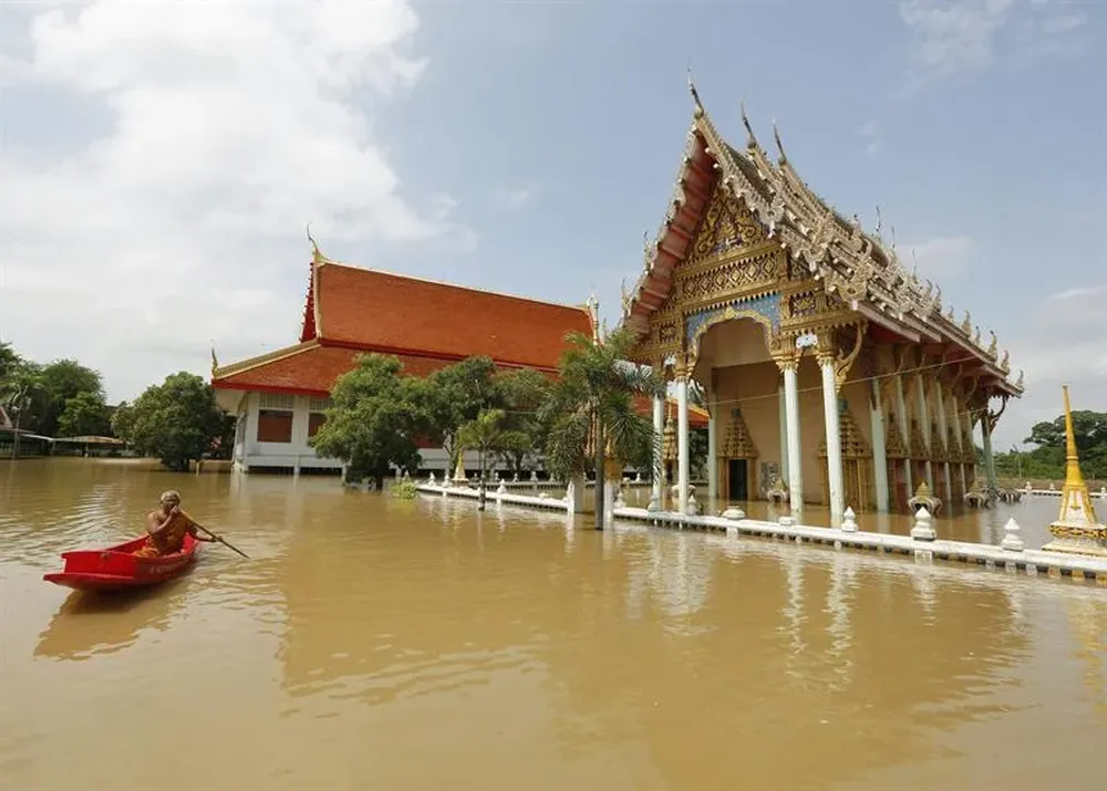 Un monje budista recorre una calle inundada subido a una pequeña embarcación en Tailandia