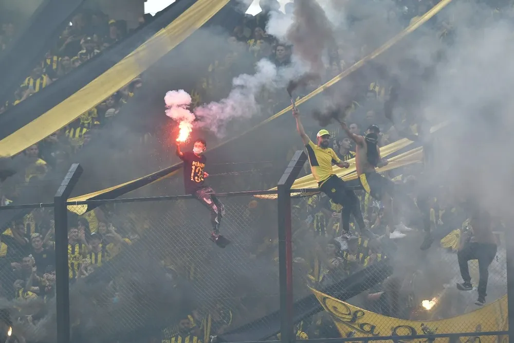 Hinchas de Peñarol subidos al tejido perimetral y con bengalas, que están prohibido encender en los estadios de fútbol
