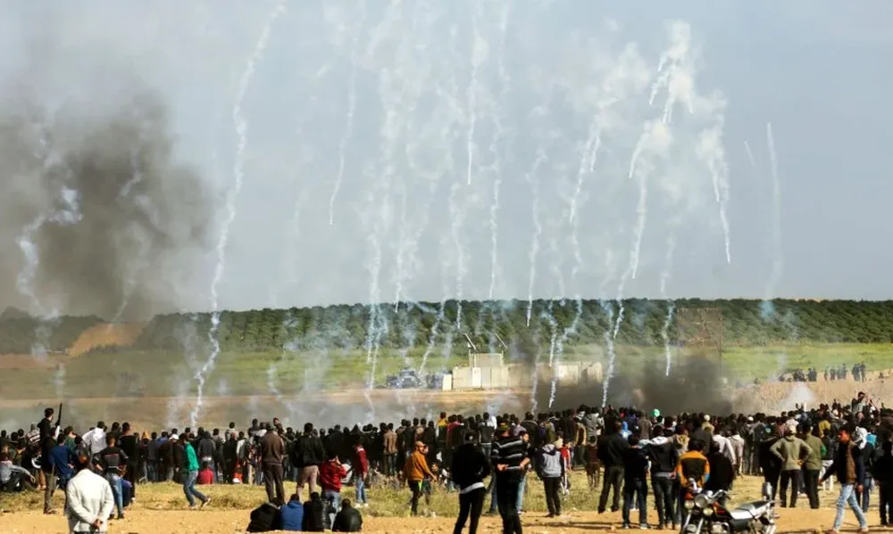 Manifestantes palestinos corren para protegerse del gas lacrimógeno lanzado por las fuerzas de seguridad israelíes