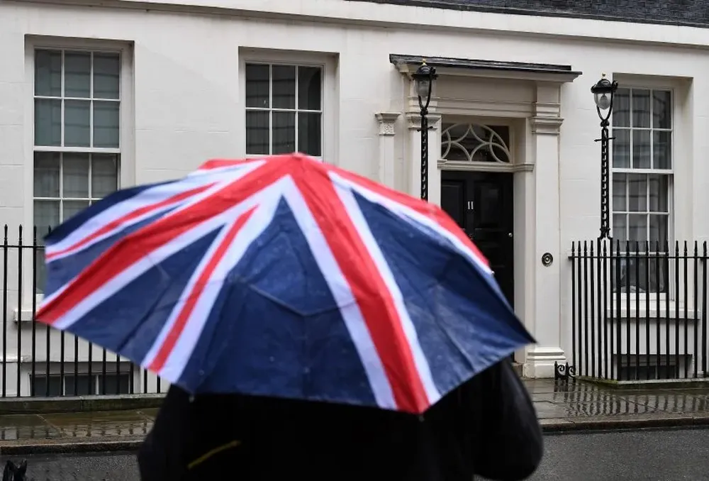 Un periodista se cubre con un paraguas frente al 11 de Downing Street