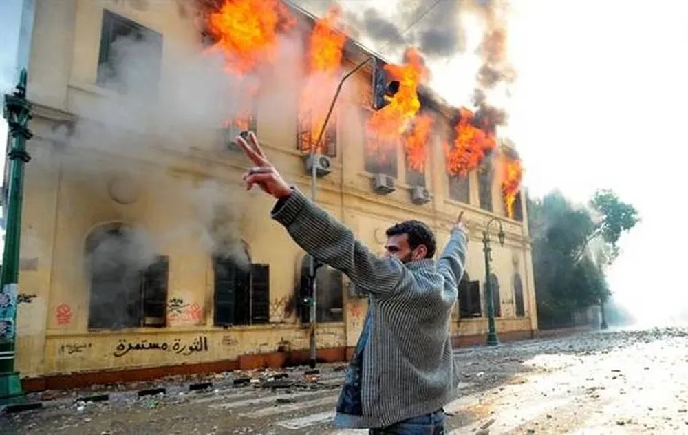 Un manifestante realiza el símbolo de la victoria frente a un edificio en llamas en El Cairo, Egipto