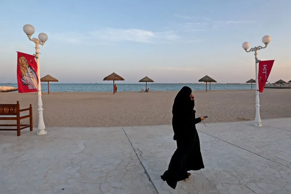 Una mujer camina frente a una playa en Doha