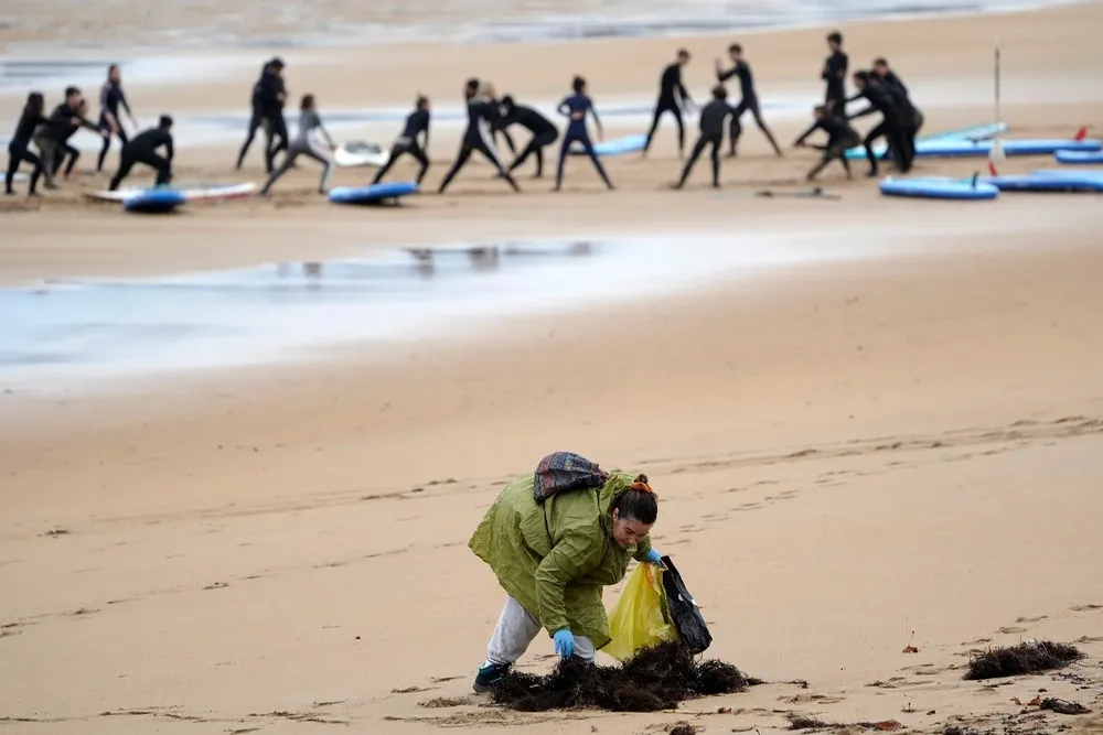 Unos voluntarios recogen pélets coordinados con Protección Civil en la playa bajo la lluvia.