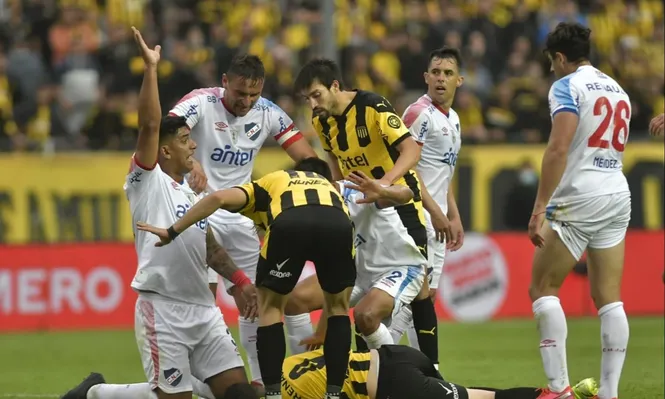 Diego Polenta levanta su mano avisándole a la sanidad de Peñarol que ingrese luego de ver al Canario Álvarez desvanecido en el suelo