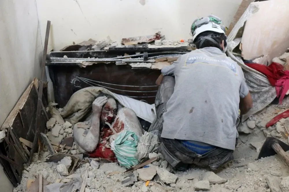 Voluntarios de protección civil de Siria los cuerpos de entre los escombros de un edificio tras un ataque.