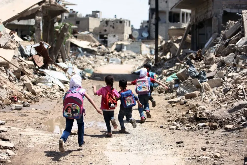 Niños sirios pasan sobre los edificios damnificados en Jobar, área tomada por rebeldes.