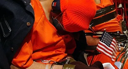 Detenidos sospechosos de pertenecer a al Qaeda o el Talibán a bordo de un avión de transporte C-141 Starlifter de las fuerzas aéreas de EE.UU. Se trata del primer vuelo que envió prisioneros desde Kandahar, en Afganistán, a la base naval de Guantánamo, en Cuba. Alguien ha colocado una bandera americana en las manos a uno de los detenidos, así como una chaqueta por los hombros, posiblemente para protegerlo del frío durante el vuelo.