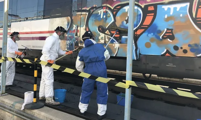 Operarios limpian un grafiti en un tren de Cercanías de Madrid.