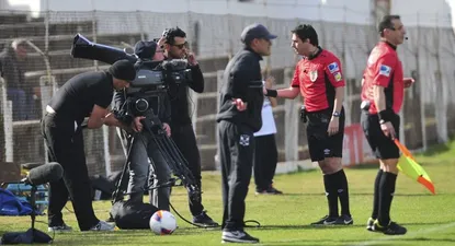 El cuarto árbitro Adrián Sánchez solicita al camarógrafo, correr su cámara hacia atrás para permitir la labor del primer asistente Carlos Pastorino