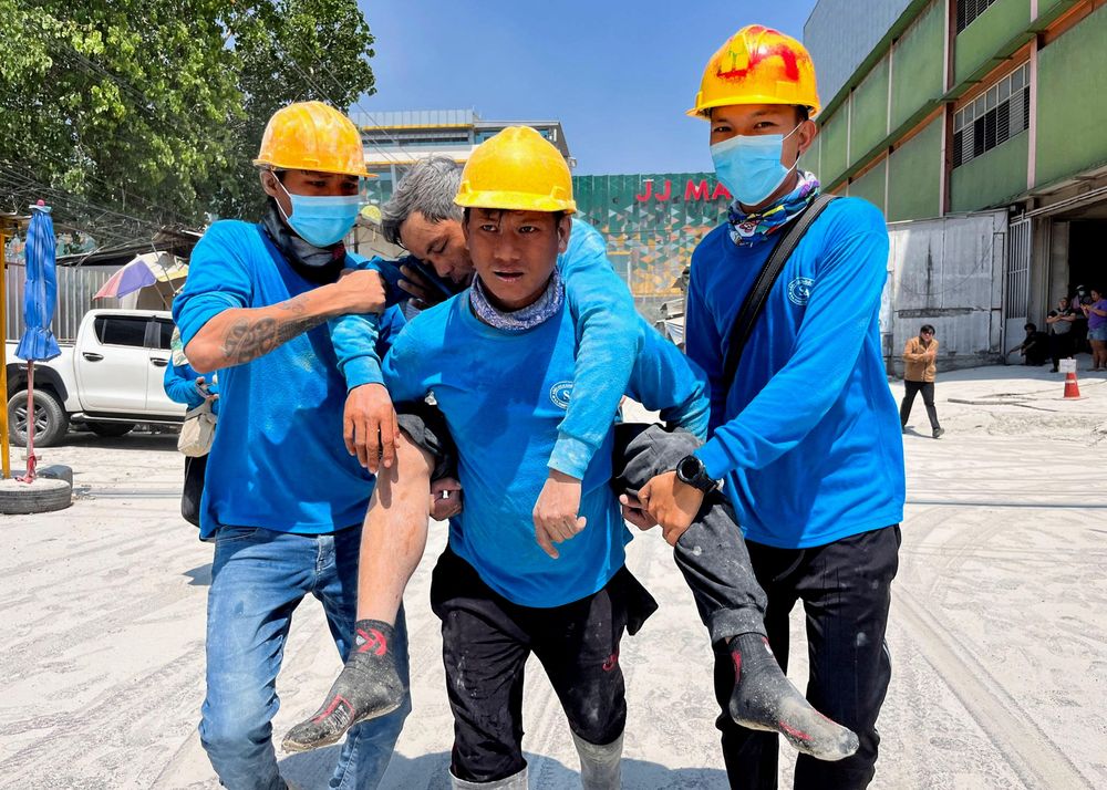 Unos trabajadores portan a un compañero herido tras derrumbarse un edificio en Bangkok.