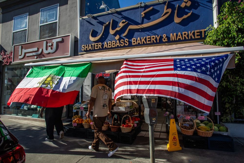 Un hombre camina por un mercado con una bandera de Irán y una estadounidense en la Plaza Persa en Los Ángeles, California.