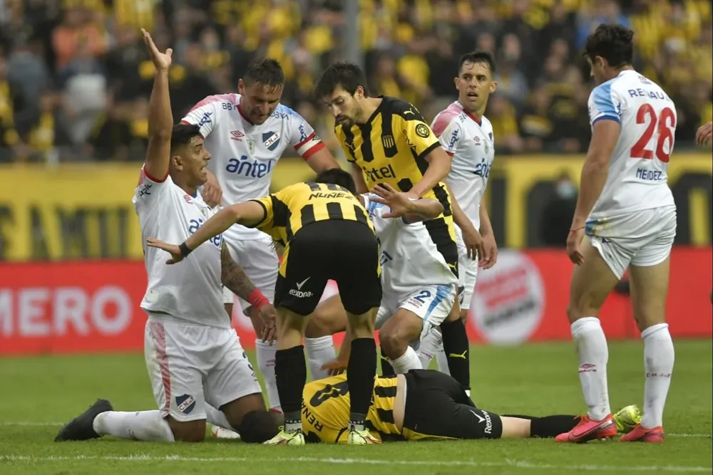 Diego Polenta levanta su mano avisándole a la sanidad de Peñarol que ingrese luego de ver al Canario Álvarez desvanecido en el suelo