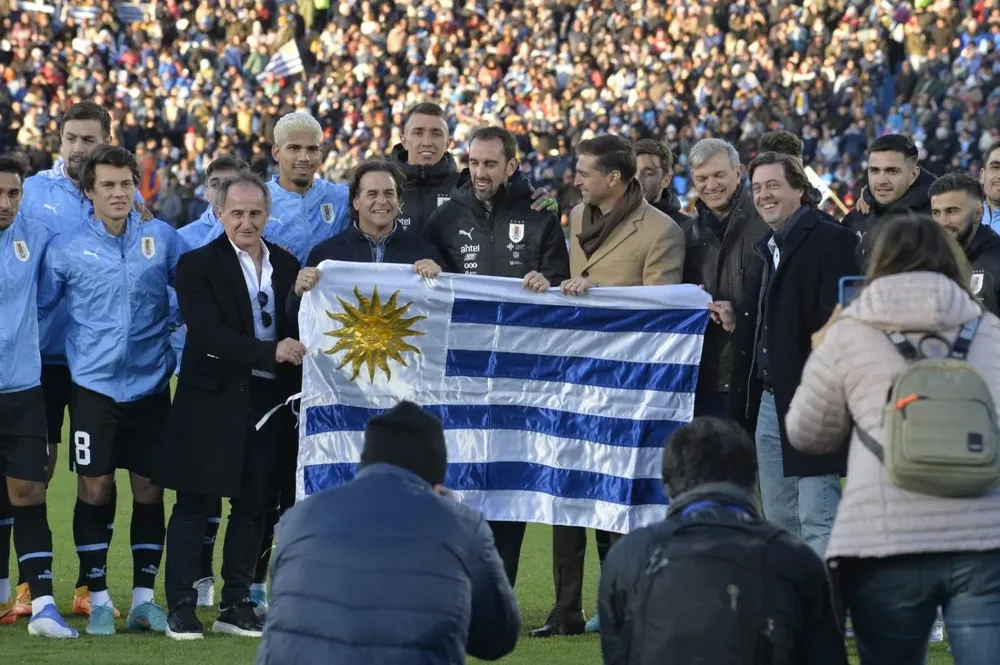 Lacalle Pou le entrega el Pabellón Nacional al capitán Diego Godín y lo acompaña el profe Ortega y Diego Alonso