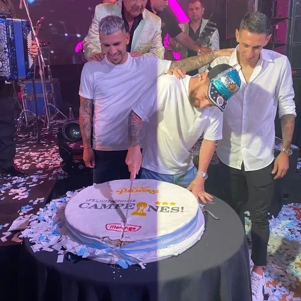 Messi corta la torta en homenaje a la obtención del Mundial, junto a Leandro Paredes (izquierda) y Ángel de María (derecha)