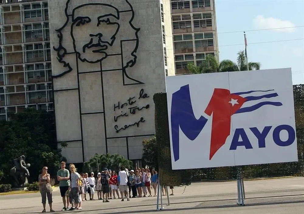 Cuba - Turistas caminan por la Plaza de la Revolución de La Habana (Cuba), junto a uno de los carteles que anuncian el desfile del 1o de mayo