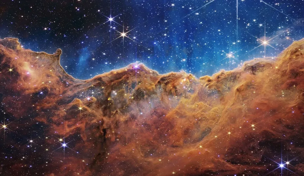 Esta imagen publicada por la NASA el 12 de julio de 2022 desde el Telescopio espacial James Webb (JWST) muestra un paisaje de montañas y valles salpicado de estrellas brillantes que en realidad es el borde de una región cercana, joven y de formación estelar. llamado NGC 3324 en la Nebulosa Carina. Capturada en luz infrarroja por el JWST, esta imagen revela por primera vez áreas de nacimiento estelar previamente invisibles.