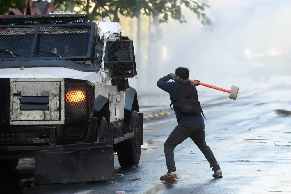 Un manifestante golpea un vehículo policial durante los incidentes en una protesta conmemorando el cuarto aniversario del estallido de 2019