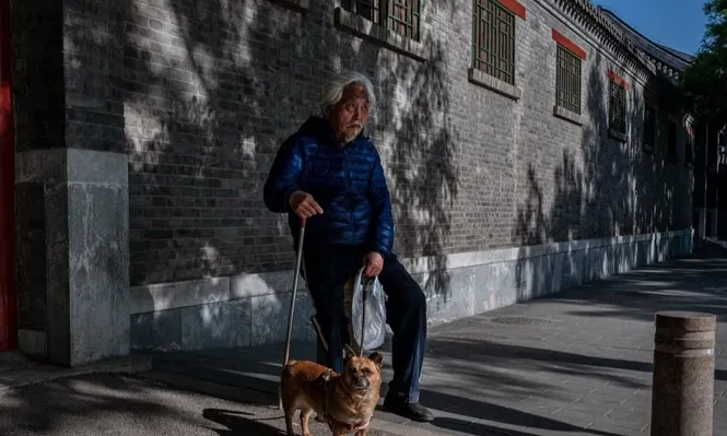 Un adulto mayor descansa y se sienta sosteniendo a su perro en una calle fuera de la Ciudad Prohibida durante el Día del Trabajo