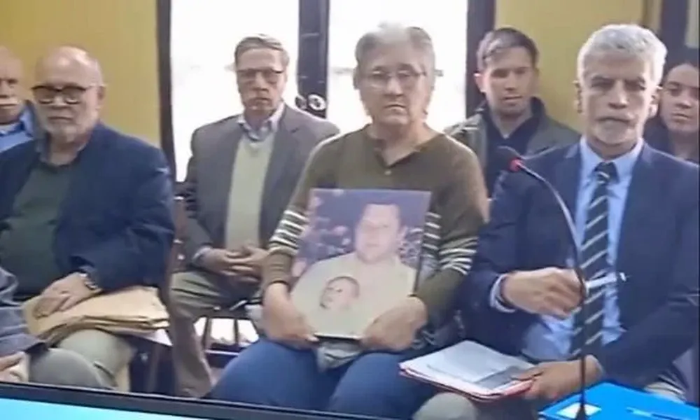 En la imagen, captura de un vídeo de la audiencia, se ve a Morales al lado de la viuda de Roslik