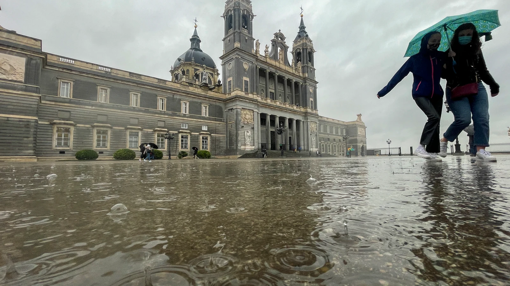 Dos mujeres caminan bajo la lluvia junto a la catedral de La Almudena en Madrid