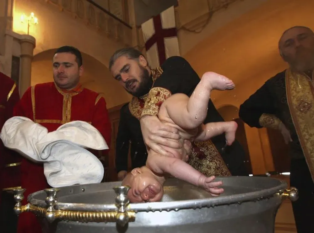 Georgia- Un sacerdote ortodoxo mete en la pila a un bebé durante un bautizo multitudinario de 900 niños