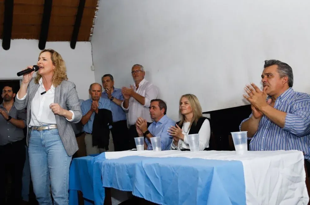 Laura Raffo da un discurso en Solymar este jueves 14 de diciembre; detrás y sentados en una mesa están el presidente de la Cámara de Diputados, Sebastián Andújar, la exfiscal Gabriela Fossati y el senador Carlos Camy