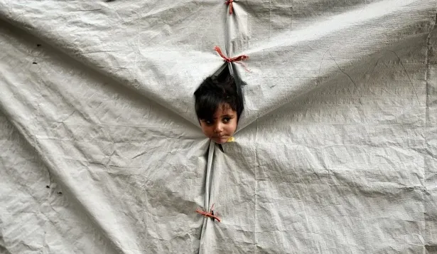 Un niño asoma la cabeza en una carpa en un campo de refugiados