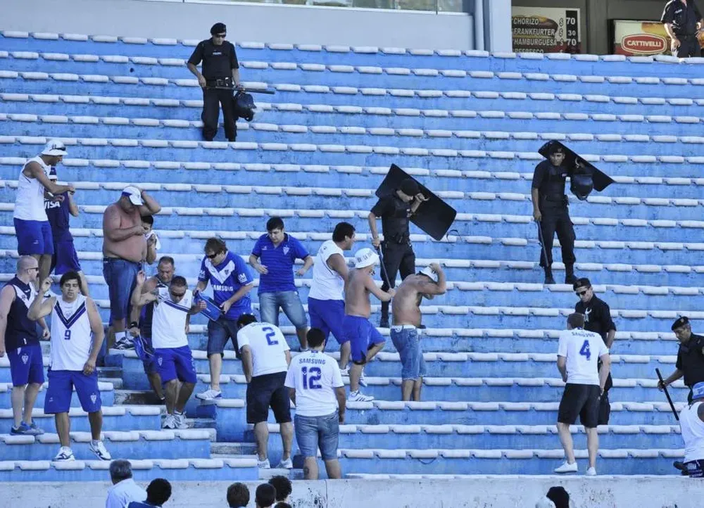 Efectivos policiales e hinchas de Velez se protegen de proyectiles que llegaban de parte de hinchas aurinegros