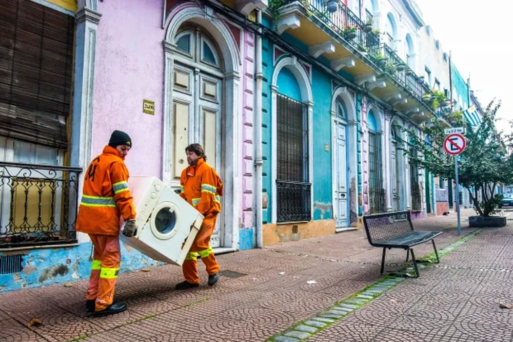 Dos funcionarios de la Intendencia de Montevideo retiran un electrodoméstico de una casa.