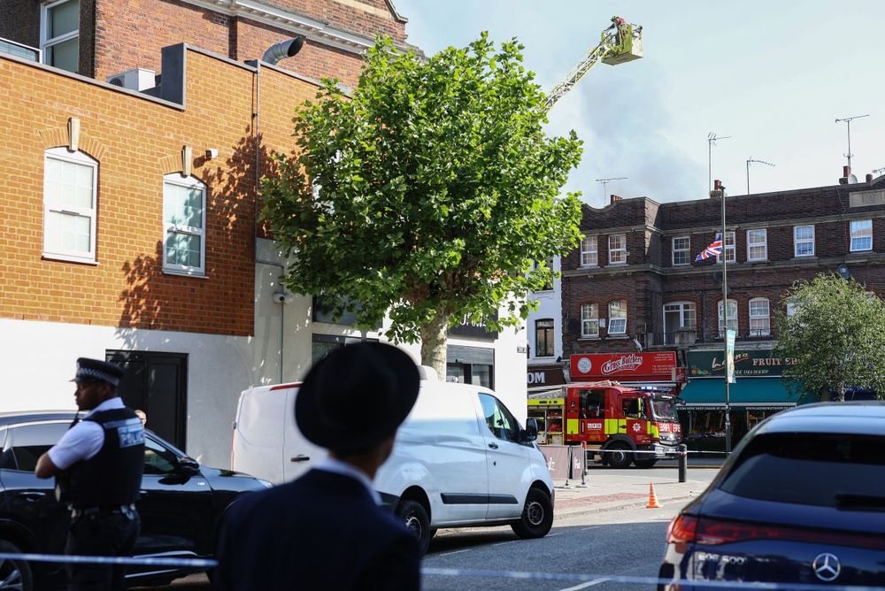 Un vecino observa mientras los servicios de emergencia (detrás) trabajan en el lugar de un incendio que se desató en un supermercado kosher en el barrio de Golders Green.