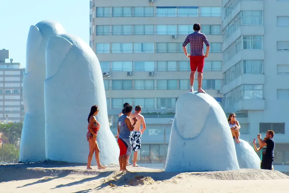 Un hombre parado sobre uno de los dedos de la escultura ubicada en la Brava de Punta del Este
