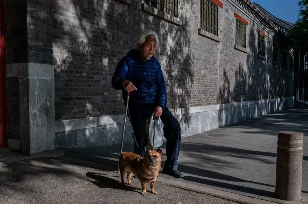 Un adulto mayor descansa y se sienta sosteniendo a su perro en una calle fuera de la Ciudad Prohibida durante el Día del Trabajo