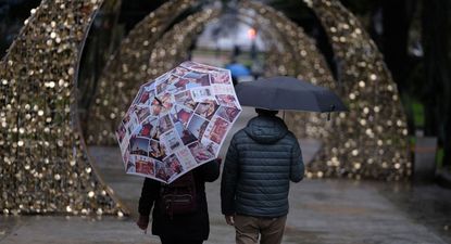 Una pareja pasea con paragüas en una calle decorada por las fiestas de fin de año