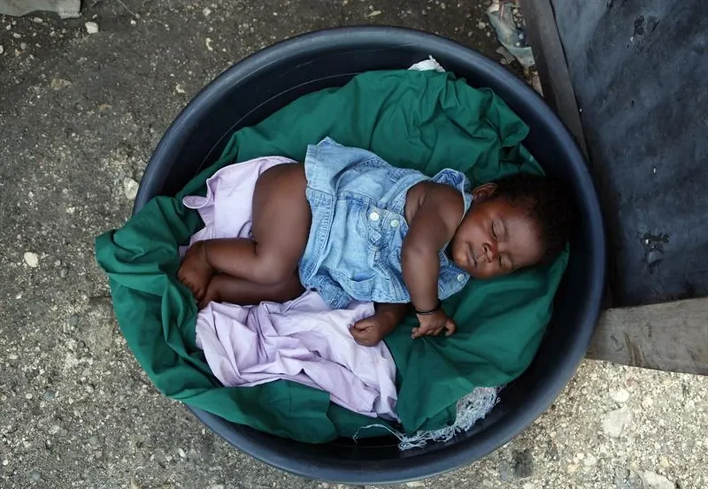 Haití- Una niña duerme en un recipiente plástico a la entrada de su carpa, en el campo de refugiados Aviación