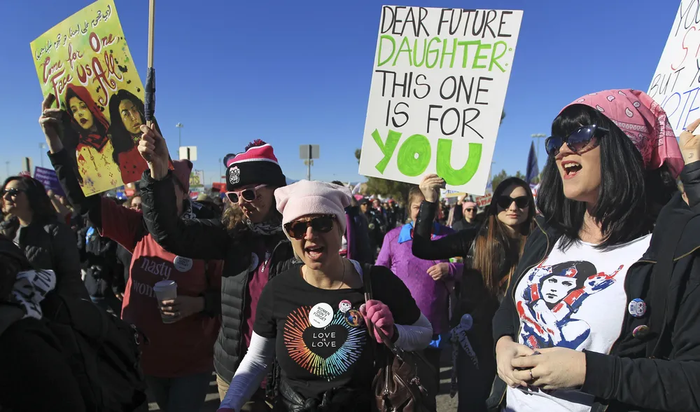 LAS VEGAS, NV - JANUARY 21: Protesters carry signs as they make their way to Sam Boyd Stadium for the Women