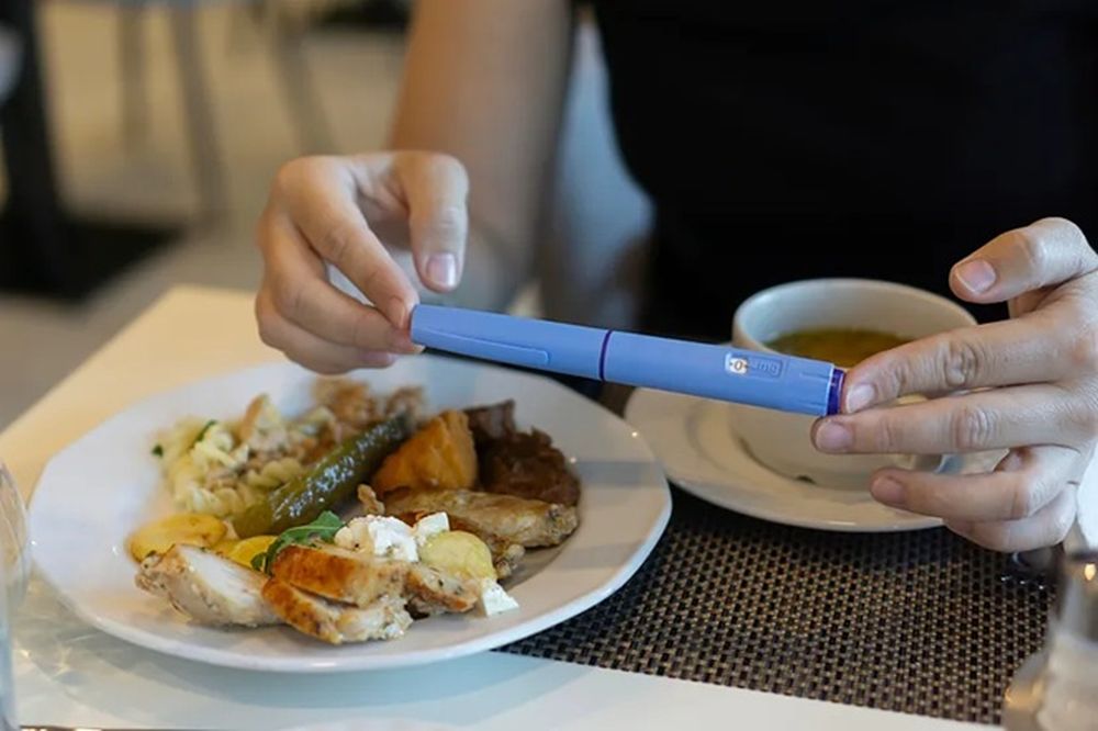 Una mujer con una dosis de Ozempic junto a un plato de comida y una taza de sopa.