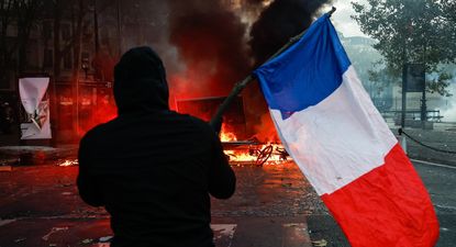 Un manifestante con una bandera francesa se enfrenta a la policía en la Plaza de la Madeleine durante una manifestación contra el aumento del coste de la vida y los recortes en los servicios públicos en París, Francia, el 17 de octubre de 2026.