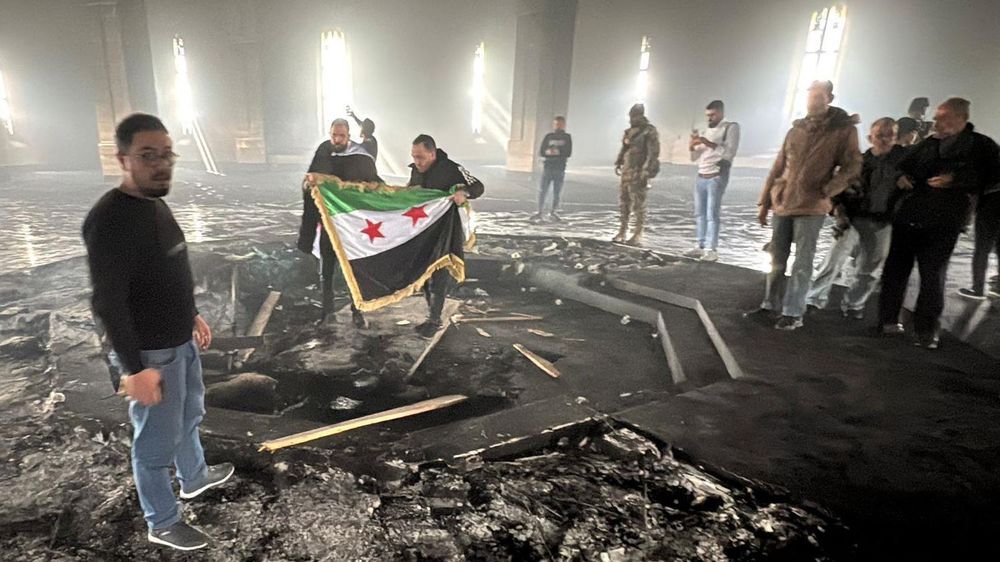 Rebeldes despliegan la bandera de la revolución siria dentro del mausoleo de Hafez al Assad, donde pueden apreciarse los rastros del fuego.