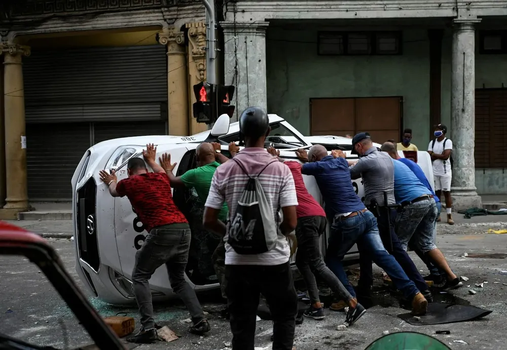 La gente empuja un automóvil volcado en la calle en el marco de una manifestación contra el presidente cubano.