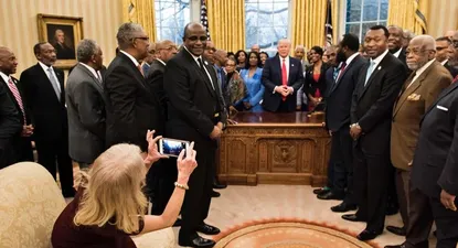 Conway, arrodillada, toma la foto de Trump con líderes de universidades y colegios negros históricos en la oficina oval.