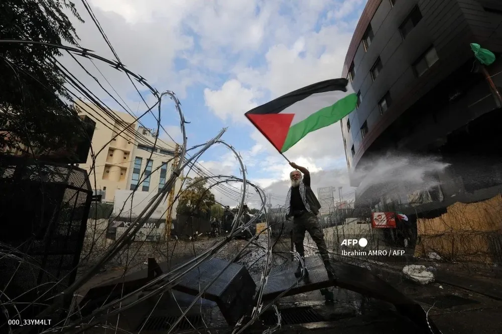 Un hombre levanta la bandera palestina mientras las fuerzas de seguridad libanesas chocan con manifestantes frente a la embajada de Estados Unidos en Beirut.