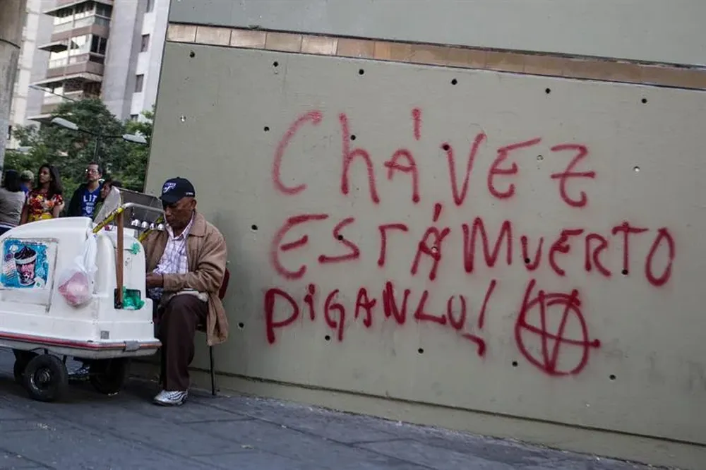 Venezuela- Un hombre vende helados cerca de un graffiti que especula con la muerte de Hugo Chávez
