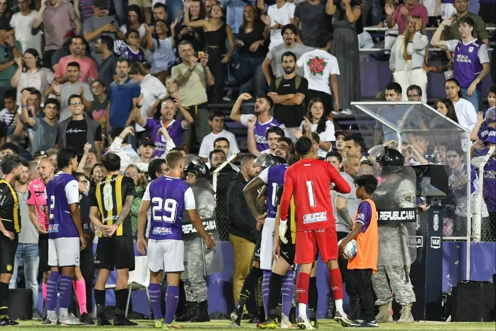 Matonte viendo el monitor del VAR rodeado de jugadores de Defensor y Peñarol
