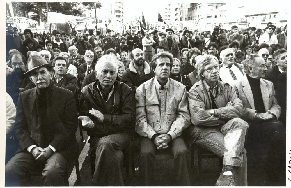 La foto que ilustra este capítulo, tomada el 1º de mayo de 1992, muestra a una parte de la dirección del Frente Amplio de entonces: de izquierda a derecha, al general Víctor Licandro; el renunciante secretario general del Partido Comunista, Jaime Pérez; el intendente de Montevideo, Tabaré Vázquez; el senador Danilo Astori; y el general Líber Seregni. Detrás pueden apreciarse, entre otros, al colorado Víctor Vaillant, quien se había sumado a la campaña pro referéndum contra la ley de empresas públicas; Wilfredo Penco, entonces jerarca municipal; y Reinaldo Gargano, senador del Partido Socialista.