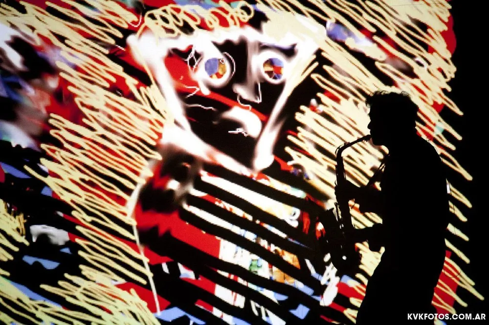 Sergio Dawi toca el saxofón con una imagen creada por Daniel “Semilla” Bucciarelli de fondo