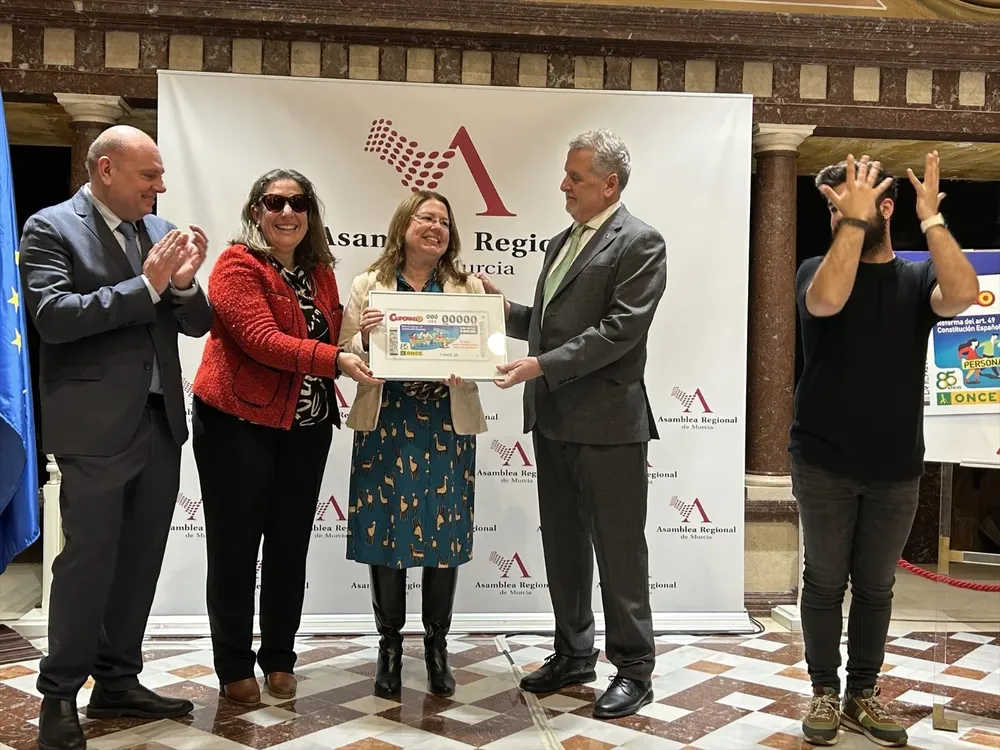 La presidenta de la Asamblea Regional, Visitación Martínez, presenta el cupón especial de la ONCE dedicado a la reforma del artículo 49 de la Constitución que ha permitido sustituir el término ‘disminuido’ por el de ‘personas con discapacidad’