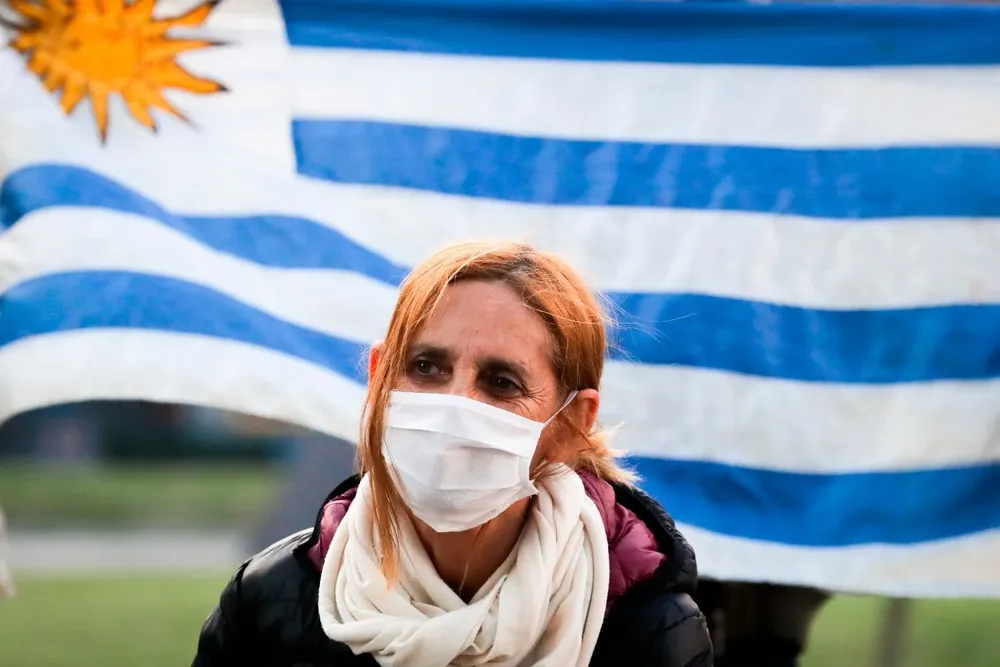 Una mujer protegida con tapabocas se ve frente a una bandera de Uruguay en Montevideo