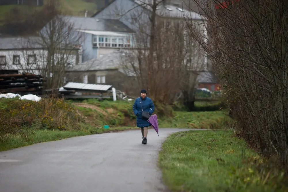 Una mujer con paraguas en un camino del municipio de Pedrafita do Cebreiro.